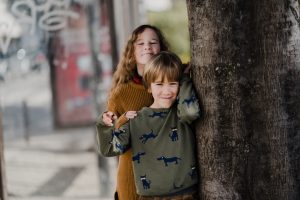 Brother and sister posing for photo beside a tree