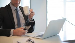 Man in black suit drinking coffee in front of laptop