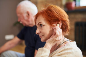 Side view of senior woman with short red hair using her hearing aid while sitting with other people in yoga class