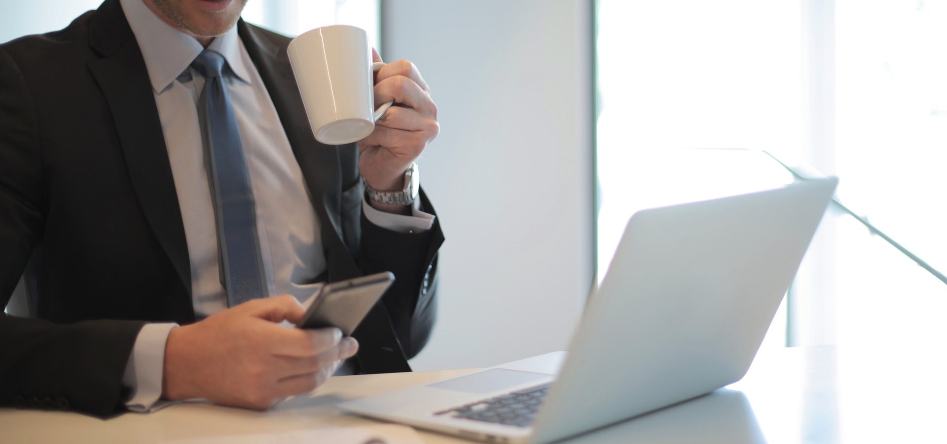 Man in black suit drinking coffee in front of laptop