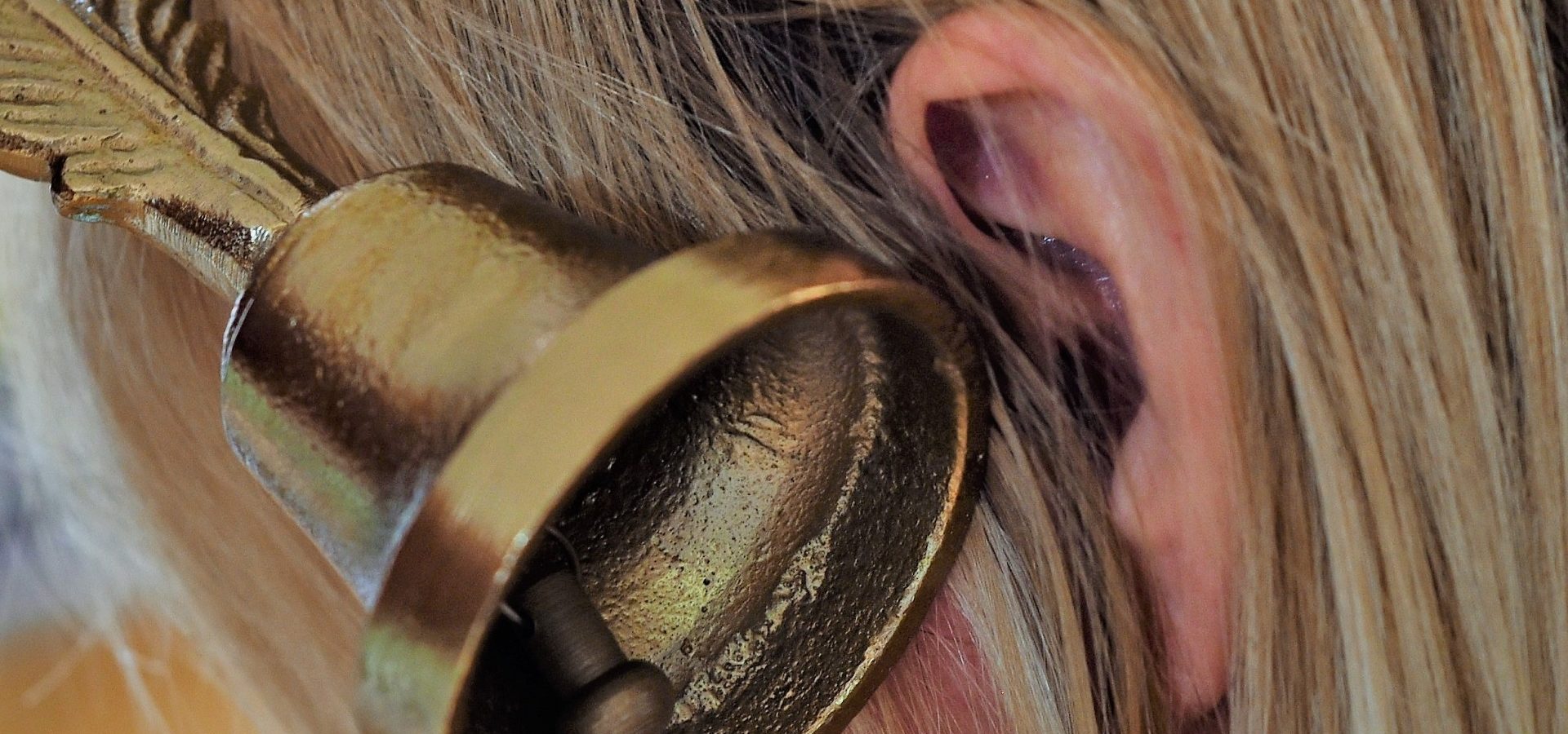 A bell placed next to a womans ear, representing the ringing sound associated with tinnitus