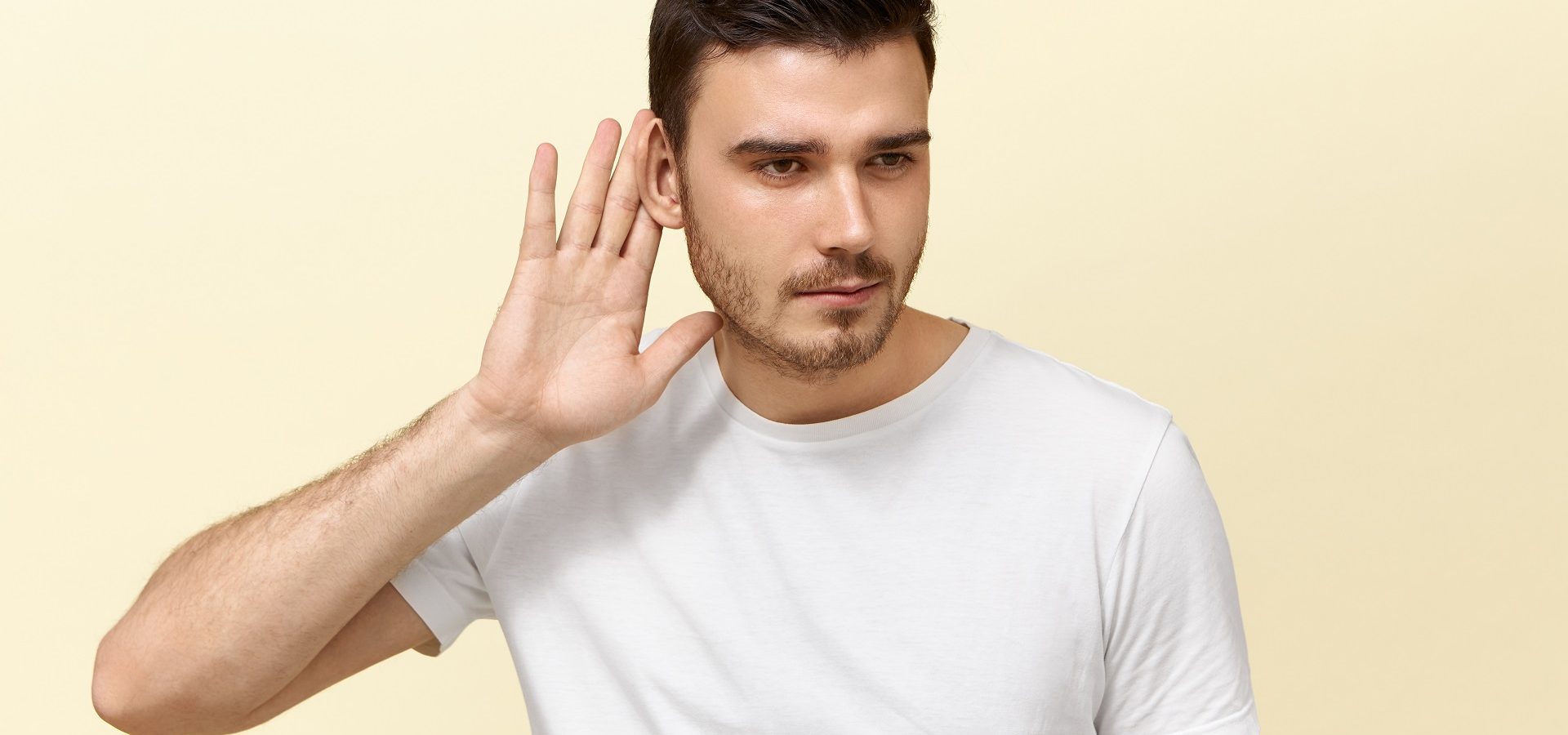 Young man holding his hand up to one ear, suffering from single-sided deafness