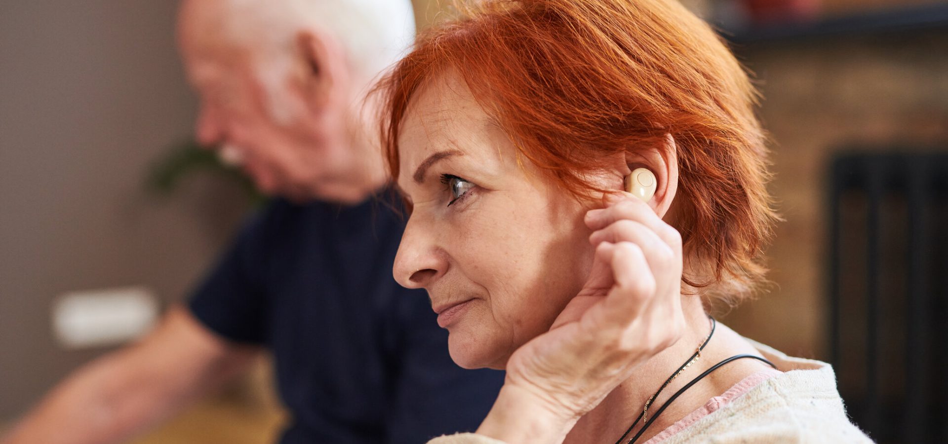 Side view of senior woman with short red hair using her hearing aid while sitting with other people in yoga class